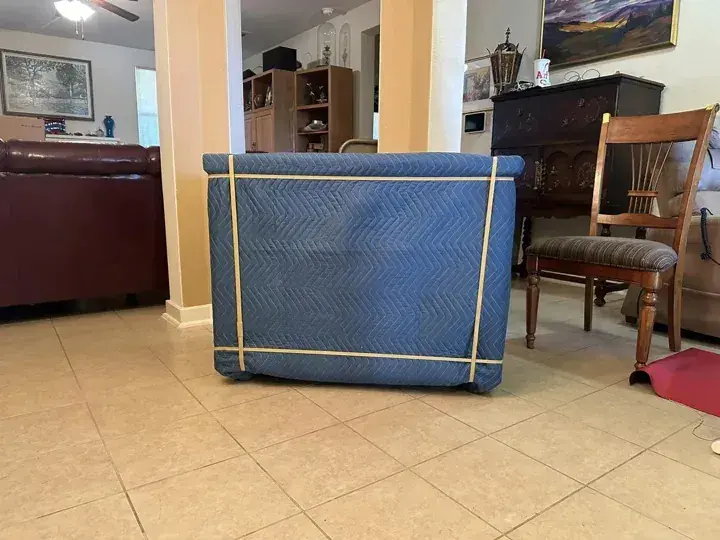Rectangular furniture piece wrapped in a blue moving pad and secured with bands