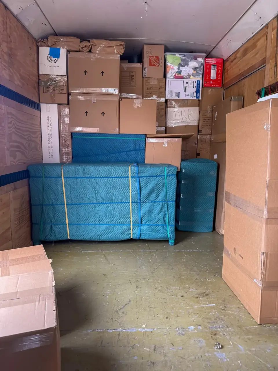 Cartons and blue padded furniture secured inside an enclosed moving trailer